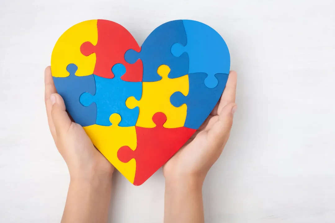 Puzzle en forme de coeur aux couleurs de l'autisme tenu par des mains d'enfant